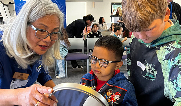 Two youth are selecting and trying on frames with the help of a volunteer at an Eyes of Hope mobile clinic outreach event.